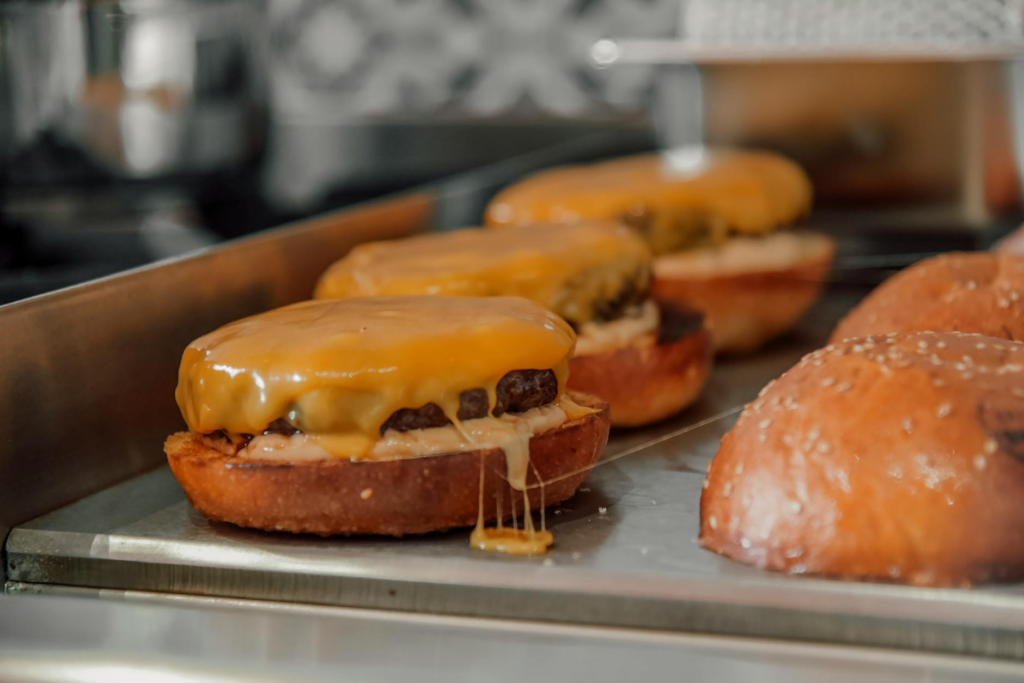 A close-up shot of a juicy burger being cooked on the grill at a local burger joint, with sizzling sounds in the backgroun…