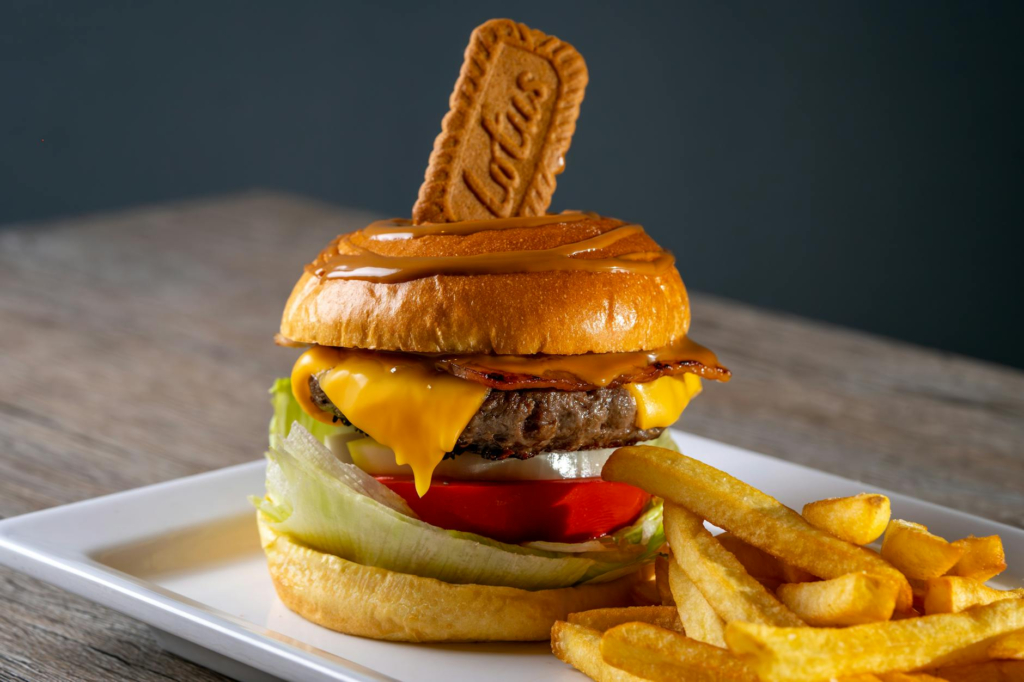 A gourmet burger with unique toppings, such as bacon-wrapped dates and blue cheese, served on a vibrant plate. — Unique …