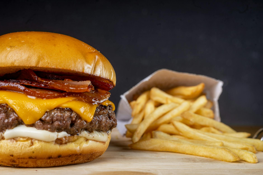 A mouthwatering burger with melted cheese and crispy bacon, served with fries on a wooden table. — late night burgers La…