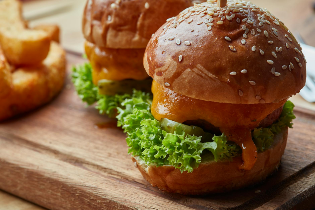 A mouthwatering cheeseburger slider with melted cheese and fresh toppings on a wooden table. — culinary scene cheeseburg…
