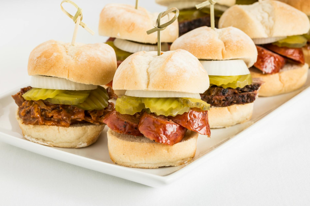 An outdoor cookout scene with cheeseburger sliders and various side dishes on a picnic table. — side dishes for cheesebu…