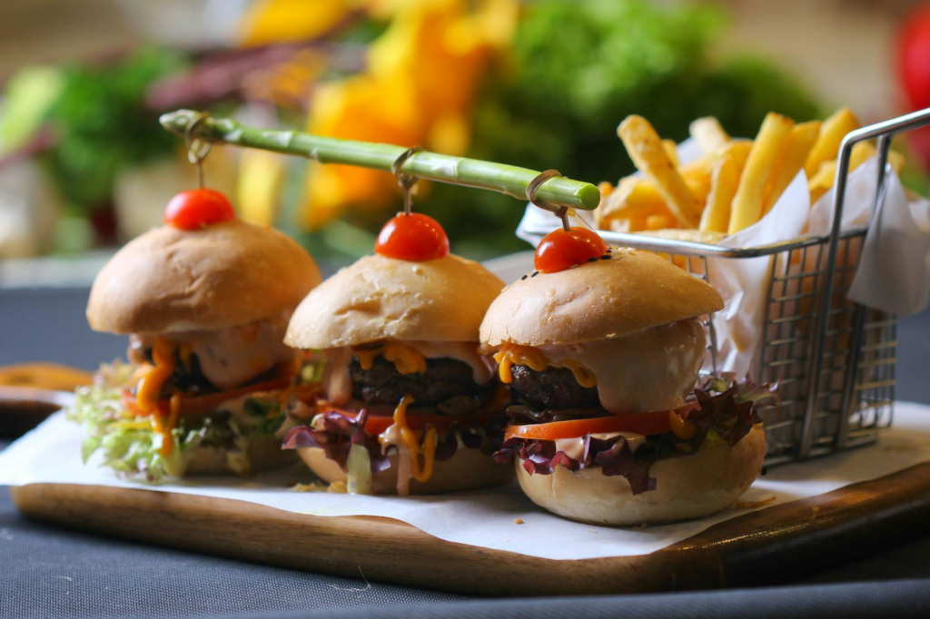 Different variations of cheeseburger sliders displayed on a rustic wooden board. — cheeseburger slider meal prep