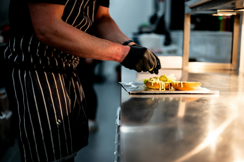 A chef preparing a gourmet burger in a high-end kitchen, highlighting the attention to detail and quality ingredients. —…