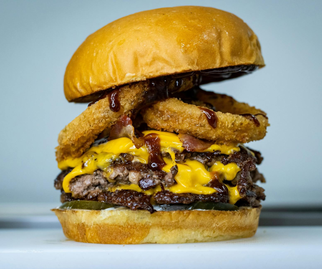 A close-up shot of a gourmet burger stacked high with toppings and sauces. — late night burgers Las Vegas