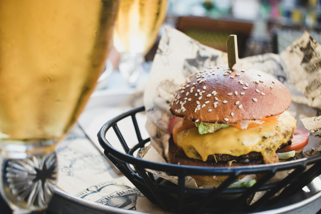 Close-up of a perfectly grilled burger topped with fresh ingredients and a pint of craft beer. — burger and beer pairing…