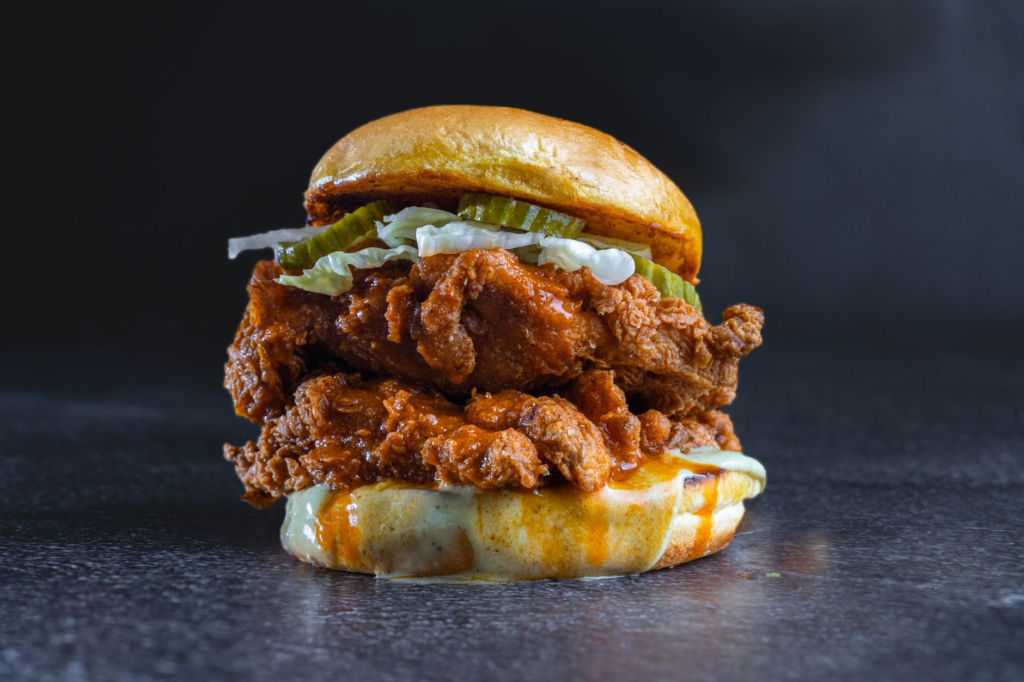 A close-up of a gourmet chicken sandwich topped with spicy sauce and pickles. — chicken burgers las vegas