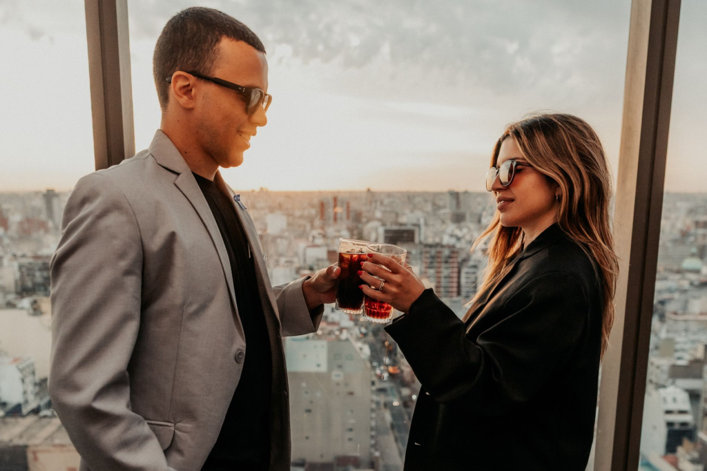 A couple toasting with drinks at a rooftop venue, with burgers and the Las Vegas skyline behind them. — burgers with a v…