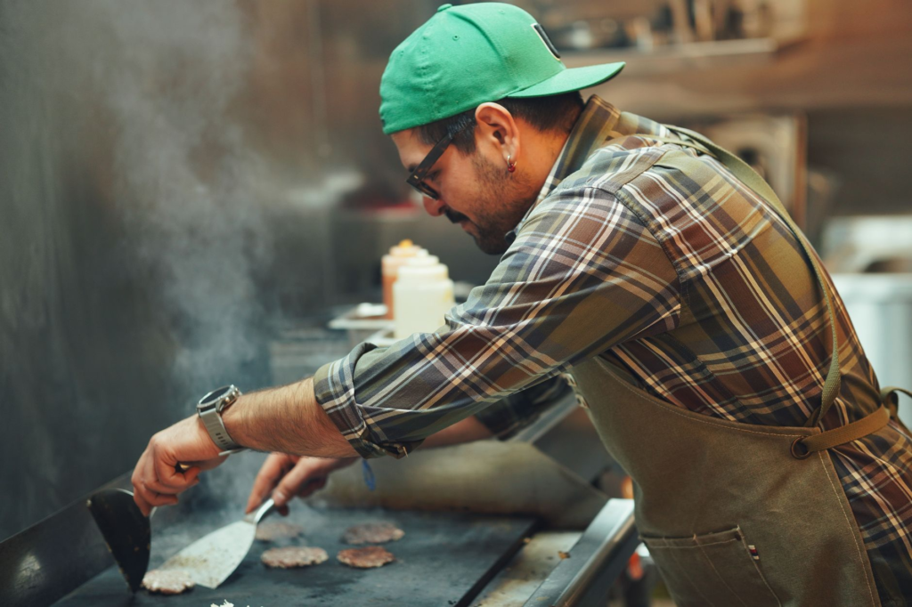 A friendly chef preparing burgers on a grill, highlighting the cooking process of the best cheeseburgers Las Vegas.