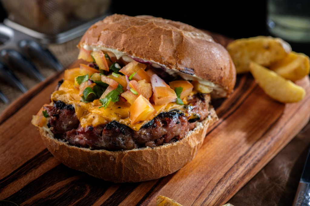 A gourmet burger with a perfectly grilled patty and fresh toppings, served on a rustic wooden platter. — gourmet burgers…