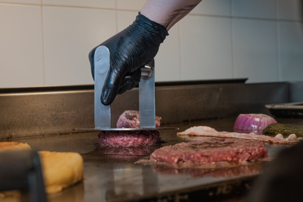 A chef preparing a traditional burger on a grill — smash burger vs regular burger