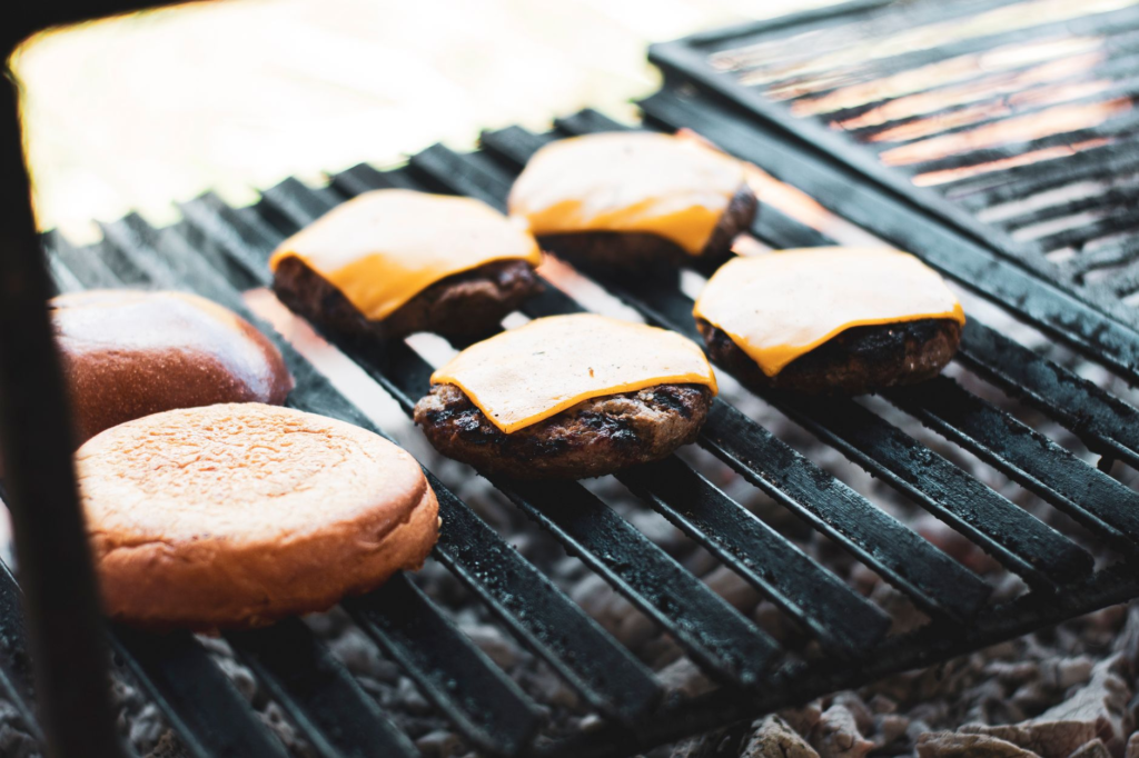 A close-up of a burger being grilled to perfection with a frosty beer in the background. — burger beer pairings Las Vegas