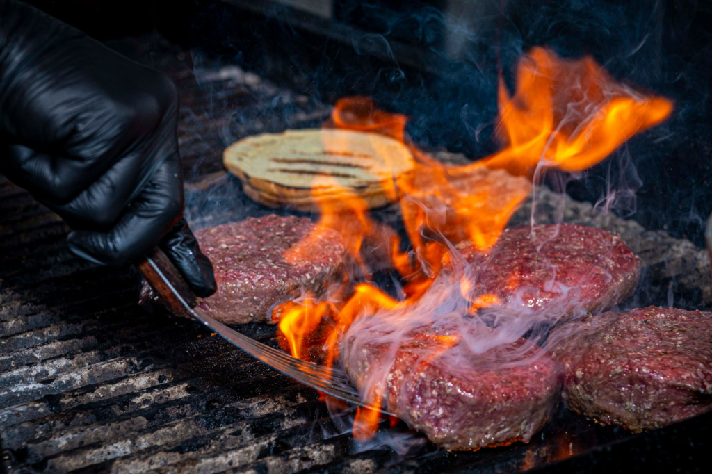 A close-up of a chef grilling burgers with flames, showcasing the preparation of spicy ingredients. — spicy burgers Las …