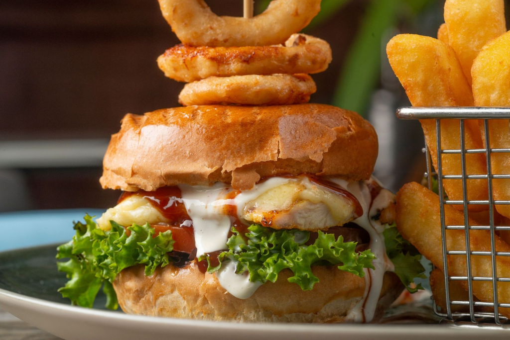 A close-up of a juicy burger being served with a side of onion rings. — burger deals Las Vegas