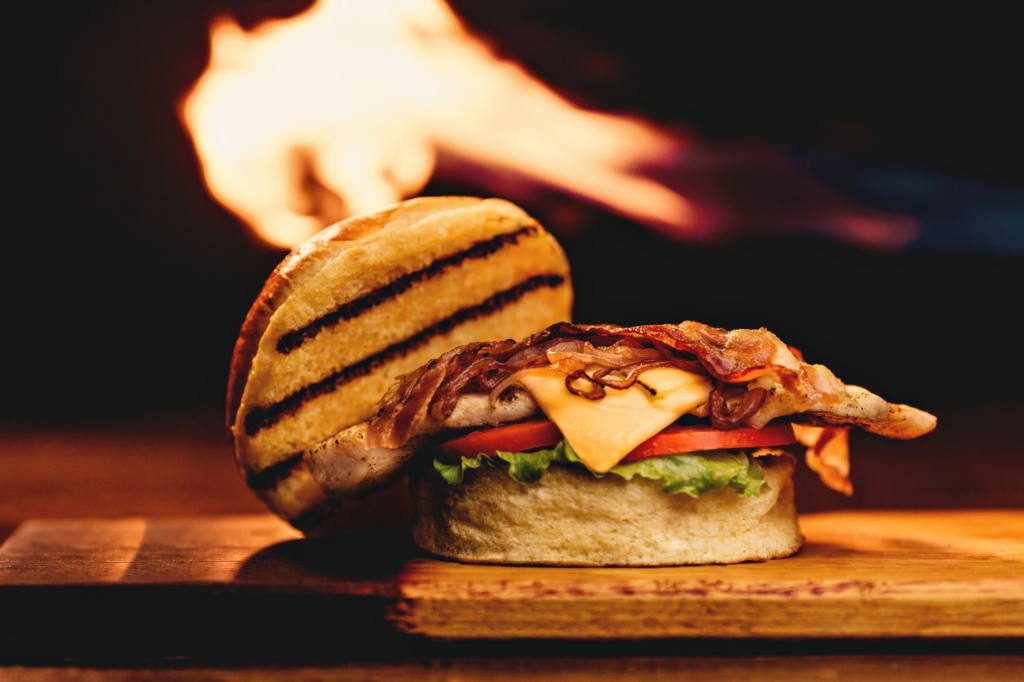 A juicy, perfectly cooked burger with toppings like lettuce, tomato, and cheese on a wooden cutting board. — what makes …